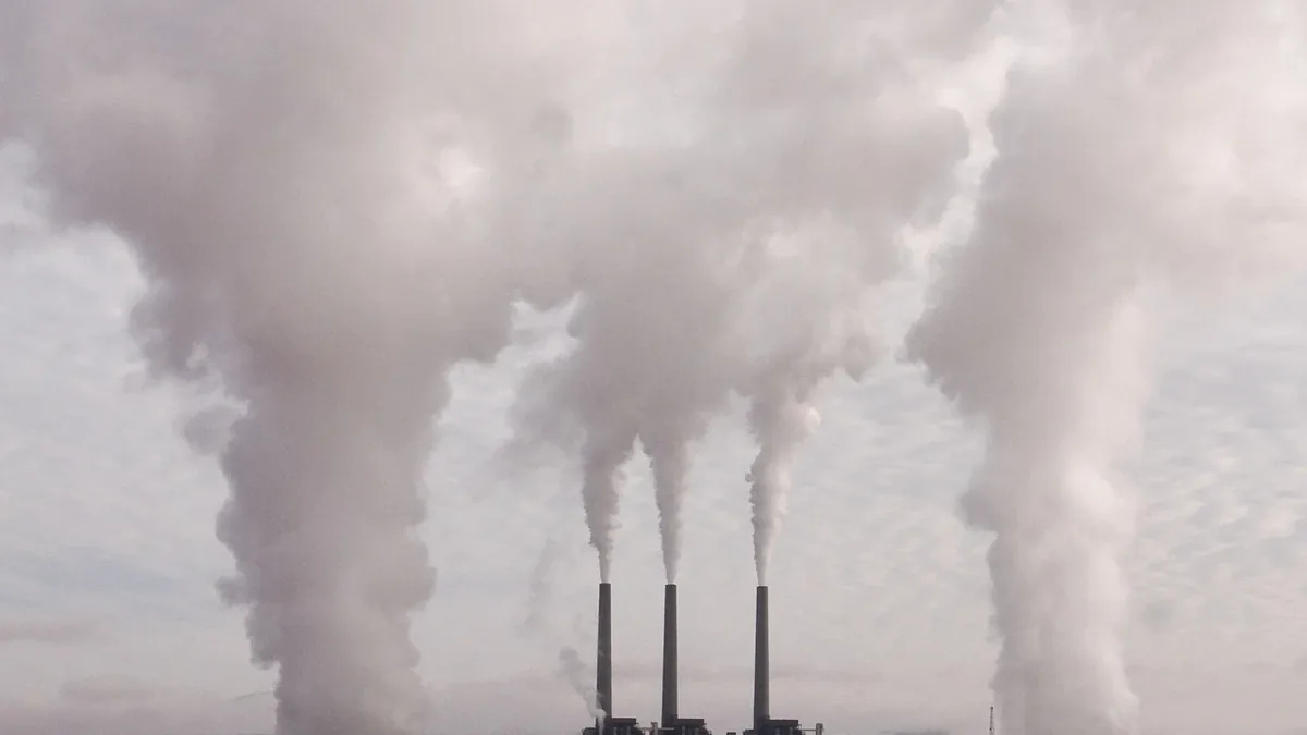 A factory emitting smoke from three tall chimneys into the air.